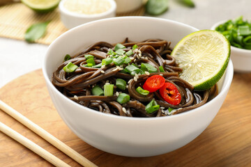 Tasty buckwheat noodles (soba) with sauce, onion in bowl and chopsticks on table, closeup