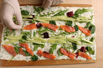 Salmon and cucumbers are added to lavash with cheese and greens. Preparation of a roll with cheese,...