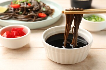 Eating delicious buckwheat noodle (soba) soup with chopsticks at white wooden table, closeup