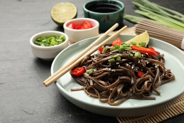 Tasty buckwheat noodles (soba) with chili pepper, onion and chopsticks on grey table, closeup