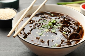 Tasty soup with buckwheat noodles (soba) and onion in bowl served on grey table, closeup
