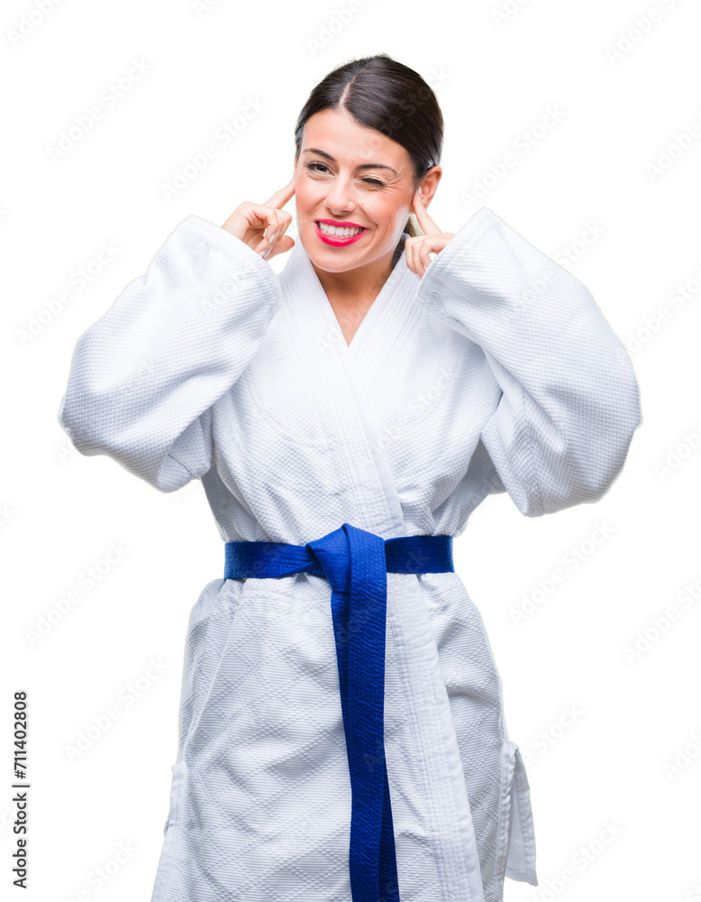 Wall mural Young beautiful woman wearing karate kimono uniform over isolated background covering ears with fingers with annoyed expression for the noise of loud music. Deaf concept.