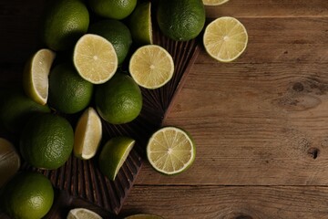 Fresh whole and cut limes on wooden table, flat lay. Space for text