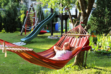 Young girl relaxing in a hammock in the garden during summer vacations. - Powered by Adobe