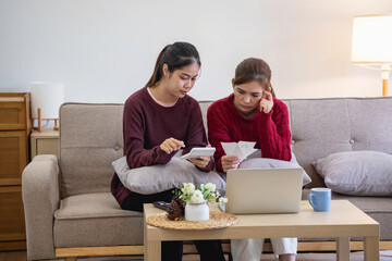 A young Asian woman sits on a sofa in her home, feeling worried and frustrated about her monthly expenses. Various utility bills.