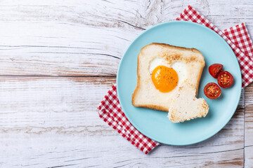 Valentine's Day breakfast with egg with tomatoes, heart shaped and toast bread on wooden table. Top...