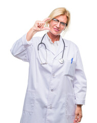 Middle age blonde doctor woman over isolated background smiling and confident gesturing with hand doing size sign with fingers while looking and the camera. Measure concept.