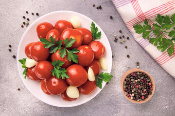 A bowl with pickled tomatoes and spices on a gray background