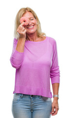 Middle age blonde woman eating pink donut over isolated background with a happy face standing and...