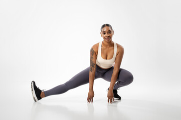 Athletic african american woman exercising stretching legs muscles, white background