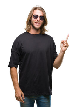 Young handsome man with long hair wearing sunglasses over isolated background with a big smile on face, pointing with hand and finger to the side looking at the camera.
