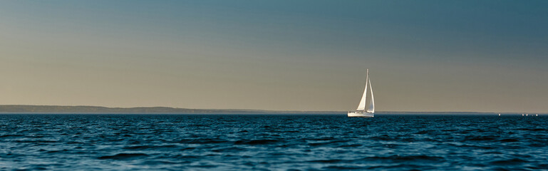 Sailing boat or yacht with open white sails floating on the sea at sunset. Majestic landscape, calm and tranquility
