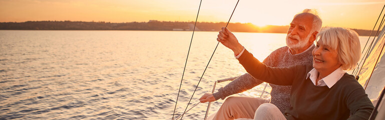 Enjoying luxury life. Beautiful happy senior couple in love relaxing on the side of sailboat or...