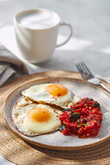 Breakfast with fried eggs and fried tomatoes with spinach on plate and cup of latte coffee
