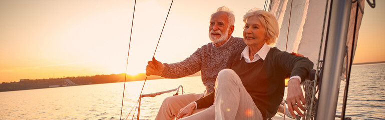 Beautiful and happy senior couple in love sitting on the side of sailboat or yacht deck floating in...