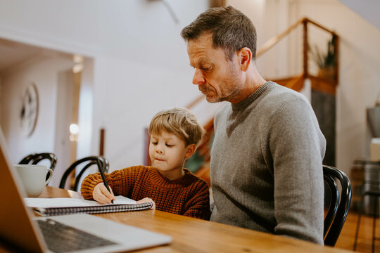 Father and young son doing homework together at table