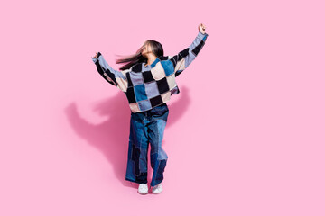 Full size photo of ecstatic lovely girl dressed jeans pullover oversize pants raising arms up dancing isolated on pink color background