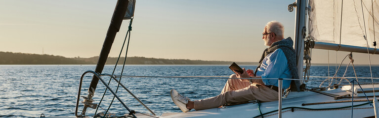 Luxury lifestyle. Side view of a relaxed senior man sitting on the side of sailboat or yacht...