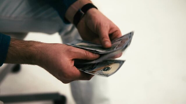The man counts the American dollars. Money in men's hands. A man holds one thousand dollars in his hands. The employee received wages in cash. Unexpected win. The fee for the work done.Time is money.