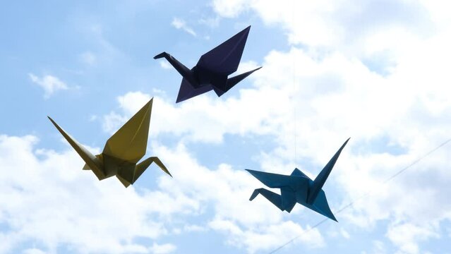 Colorful paper origami birds-cranes hang on the window against the sky. Paper birds seem to fly. Origami crane in Japanese style is a symbol of happiness and prosperity.