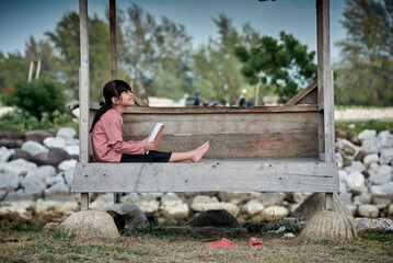 A cute little girl reading a book at a wooden gazebo outdoors
