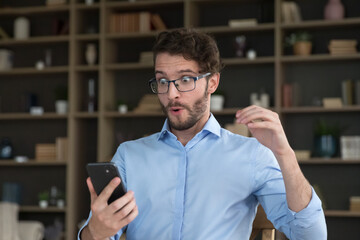 Stunned amazed guy staring at smartphone screen, goggle his eyes while read received message with great, unbelievable news, get fantastic sell-out, huge discount commercial offer, on-line lottery win