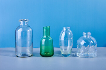 Set of various muted colored glass and metal bottles and vases on a blue background.
