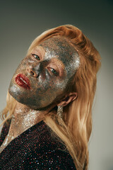 alluring young woman with green eyes and glitter all over body and face posing on grey backdrop