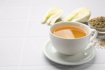 Fennel tea in cup, seeds and fresh vegetable on white tiled table, closeup. Space for text