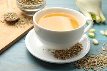 Fennel tea in cup, seeds and fresh vegetable on light blue wooden table, closeup