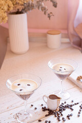 Espresso Martini cocktail in a martini glass decorated with coffee beans and a small jug with coffee liqueur in a bright interior
