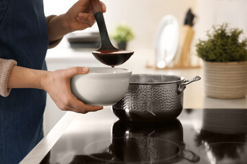 Woman pouring tasty soup into bowl at countertop in kitchen, closeup
