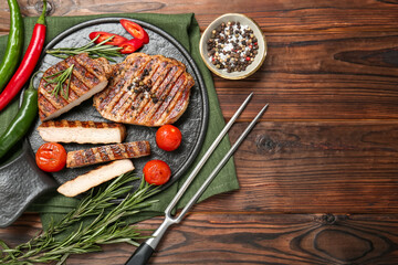 Grilled pork steaks with rosemary, spices, vegetables and carving fork on wooden table, top view....