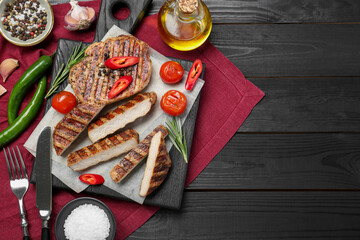 Grilled pork steaks with rosemary, spices, vegetables and cutlery on dark wooden table, top view. Space for text