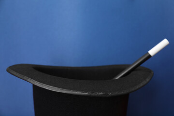 Black magician top hat and wand on blue background, closeup. Space for text