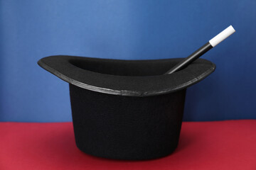 Black top hat and wand on color background. Magician equipment