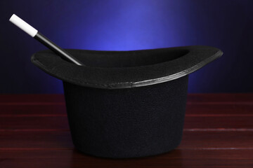 Black top hat and wand on wooden table against color background, closeup. Magician equipment