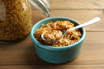 Whole grain mustard in bowl and spoon on wooden table