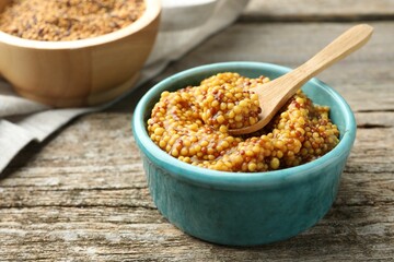 Fresh whole grain mustard in bowl and spoon on wooden table. Space for text