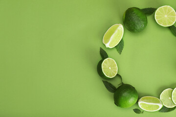 Flat lay composition with fresh limes and leaves on green background. Space for text
