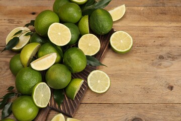 Fresh limes and green leaves on wooden table, above view. Space for text