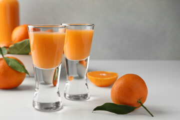 Tasty tangerine liqueur in shot glasses and fresh fruits on white table, closeup. Space for text