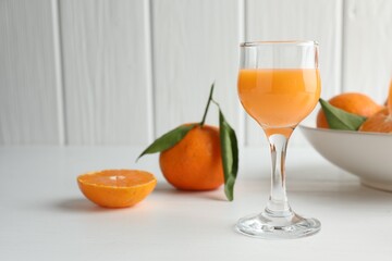 Tasty tangerine liqueur in glass and fresh citrus fruits on white table. Space for text