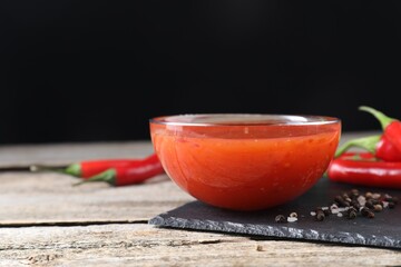 Spicy chili sauce in bowl on wooden table. Space for text