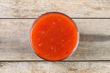 Spicy chili sauce in bowl on wooden table, top view