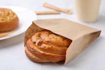 Delicious roll with raisins in paper bag on white table, closeup. Sweet bun