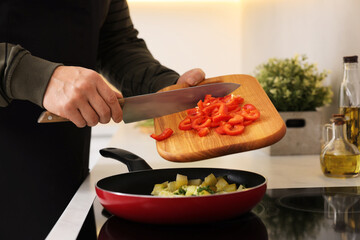 Cooking process. Man adding cut bell pepper into frying pan in kitchen, closeup