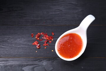 Chili sauce in spoon on black wooden table, top view