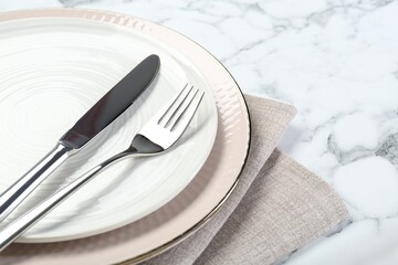 Clean plates, cutlery and napkin on white marble table, closeup. Space for text