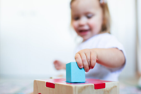 Toddler posting coloured shapes into wooden shape sorter box